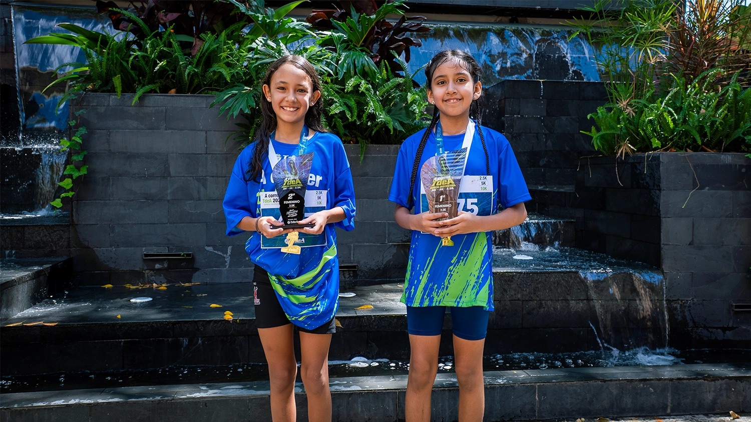Dos niñas que participaron de la carrera atlética posan con sus trofeos de primer y segundo puesto.